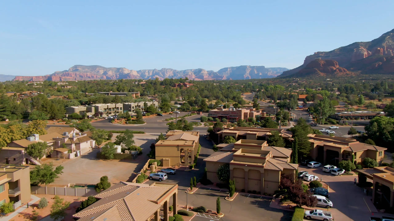 Sedona aerial view with foreground rooftops, roads, trees, and distant red rock range.