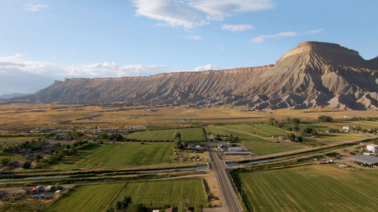 Palisades, Colorado landscape with the road centered lower in frame, rectangular fields across the foreground, a few structures in the midground, and no visible people.