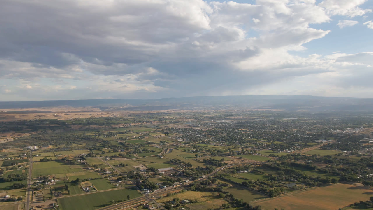 High aerial view across Palisades, Colorado, with rural fields in the foreground, settlement in the midground, low mountains on the horizon, and no visible people.