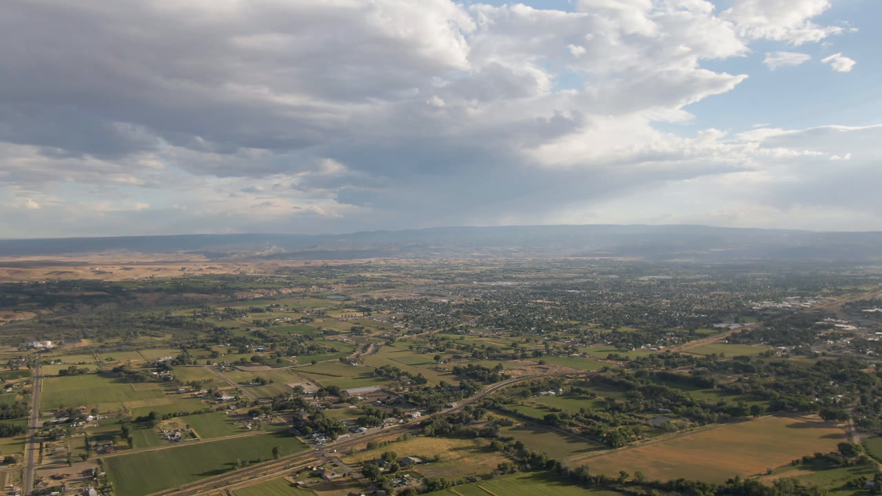 Third frame shows Palisades, Colorado from above with tan fields in the lower frame, greener parcels and buildings across the center, distant mountains, broken cloud light, and no visible people.