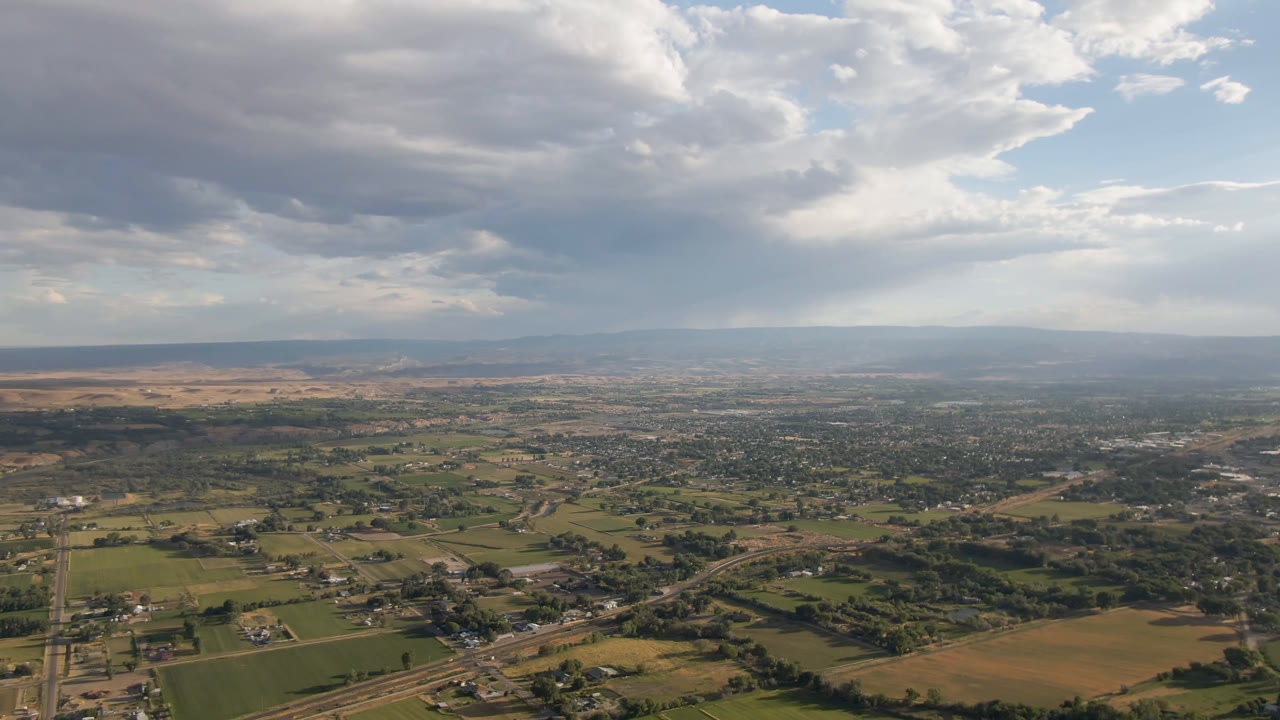 Wide overhead view of farmland and town under thick clouds with a distant horizon.