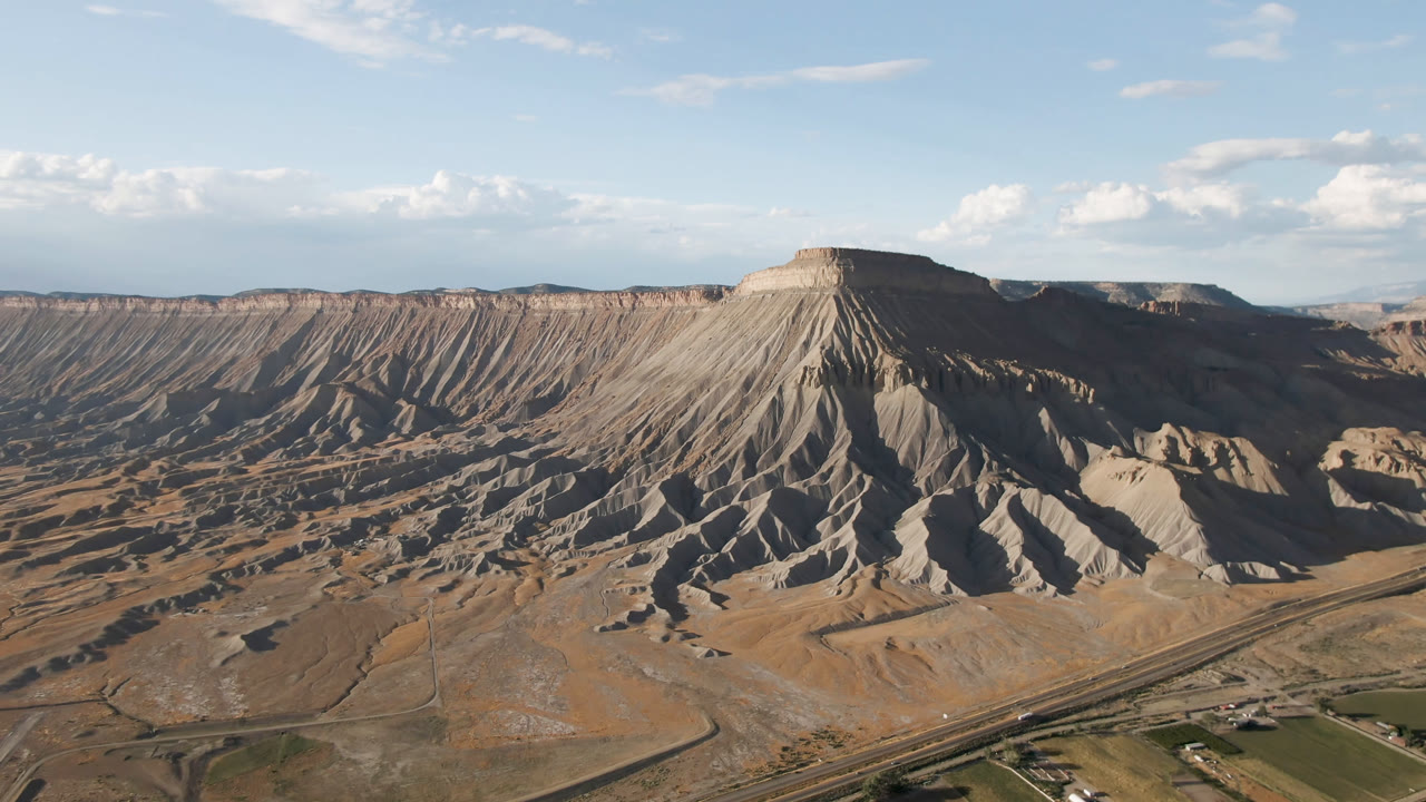Second frame of the Palisades, Colorado aerial, showing the mesa still dominant with long ridged slopes, a valley road network near the bottom edge, and no visible people.