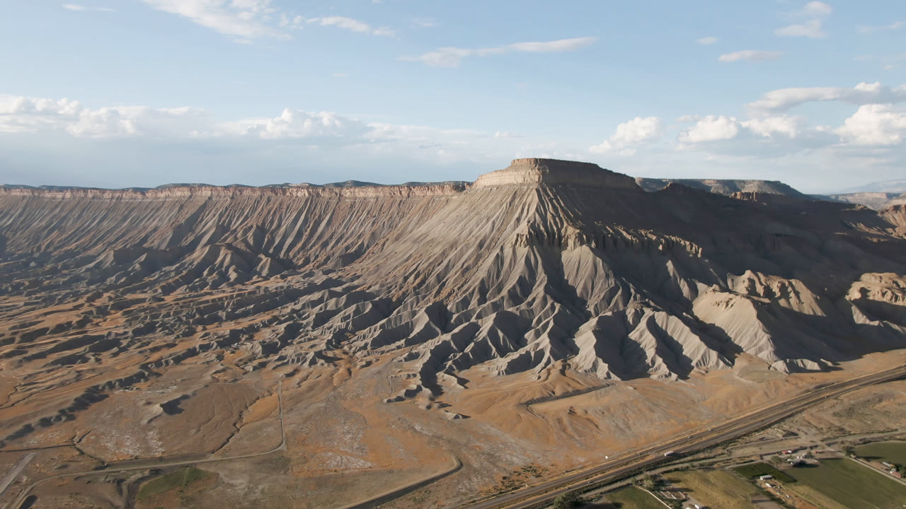 Third frame over Palisades, Colorado, with shadowed gullies cutting down the mesa face, open dry terrain across the valley, distant ridges, and no visible people.