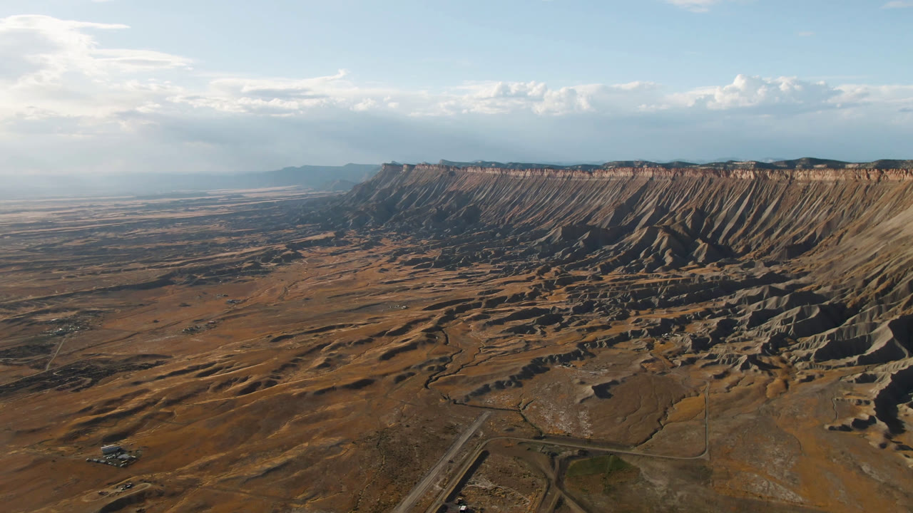 Wide aerial view of desert plateau, roads, mesa ridge, and blue sky