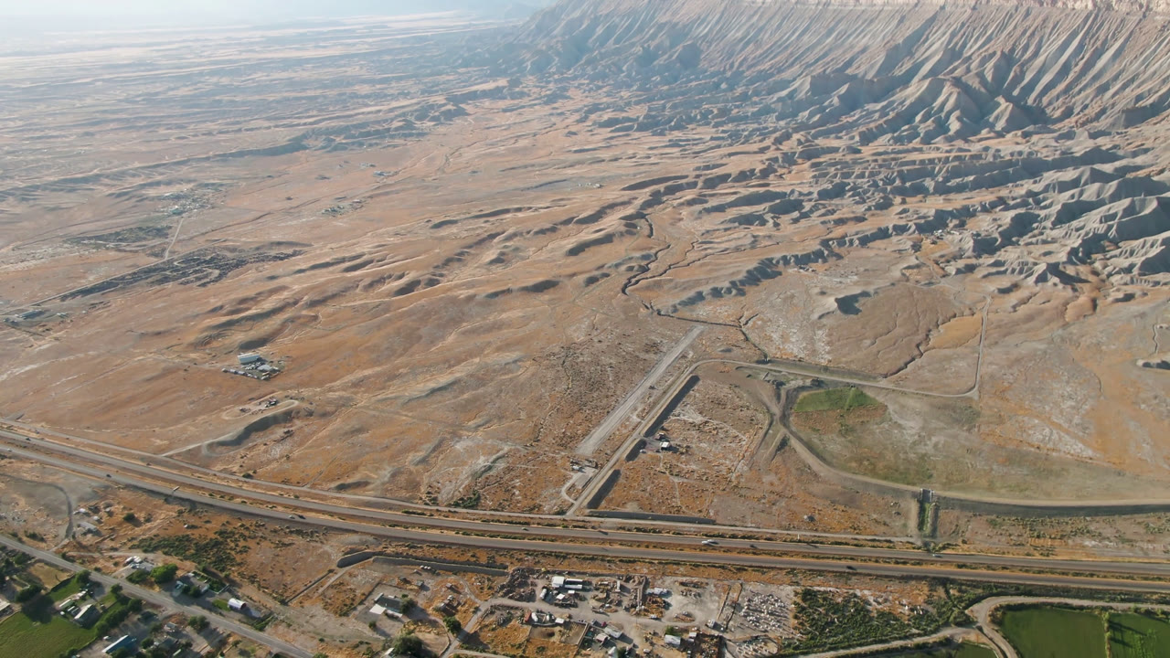 At 0:02, the Palisades, Colorado view shows road corridors across the bottom third, scattered structures near the lower edge, dry washes, and a long mountain ridge with no visible people.