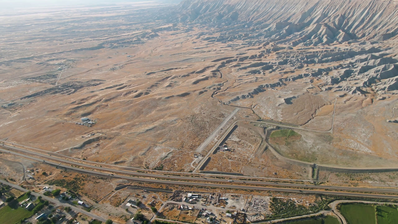 Halfway through the clip, the aerial over Palisades, Colorado shows a diagonal road, a multi-lane highway, broad sandy ground, and rugged shadowed mountain folds with no visible people.