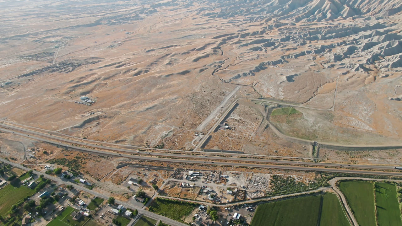 High aerial view over Palisades, Colorado, showing a highway, intersecting roads, green fields, scattered buildings, tan desert ground, and no visible people.