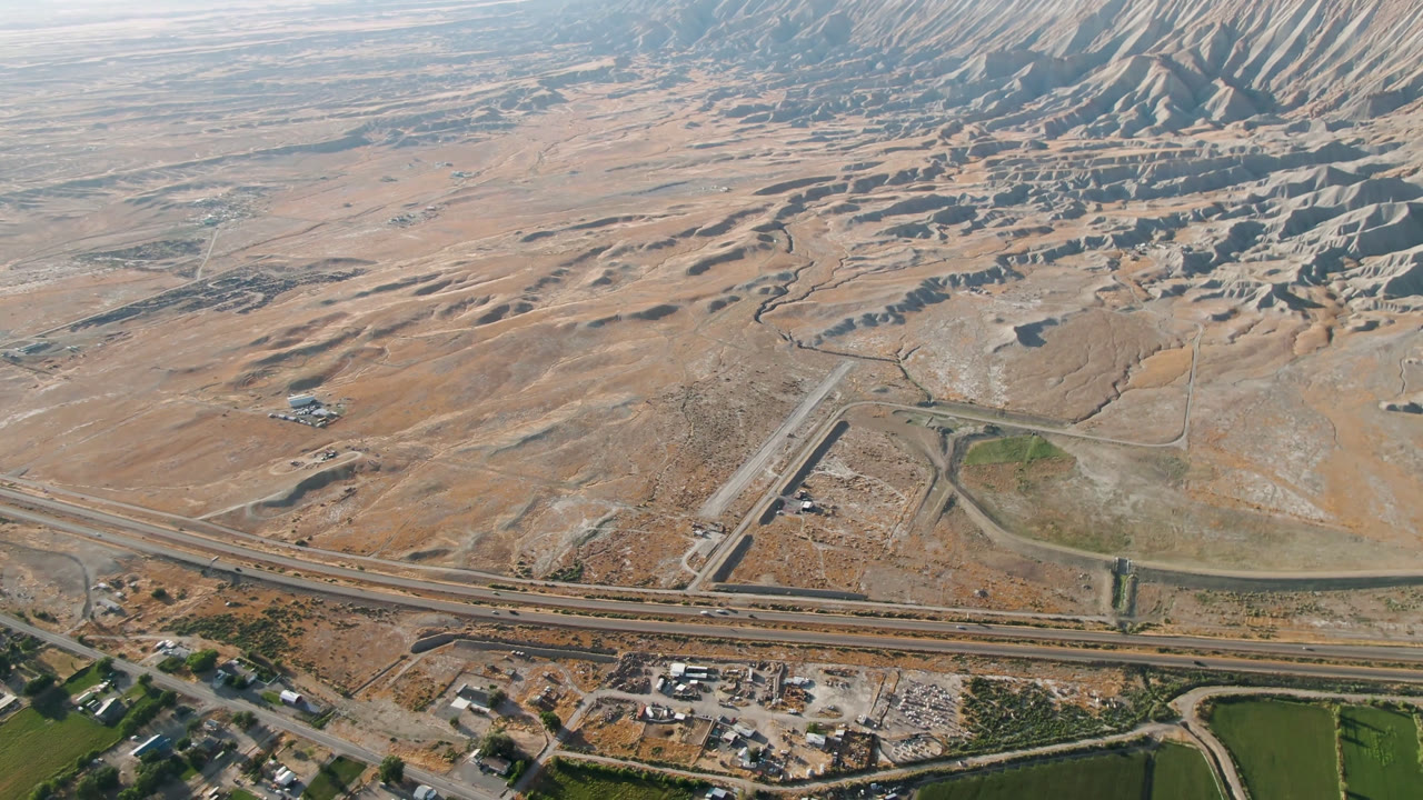 High aerial frame over Palisades, Colorado showing a divided highway, arid foothills, scattered buildings, green field edges, and no visible people.