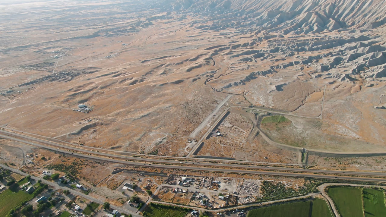 Aerial view of highway ramps, tan desert terrain, and ridged hills in the distance.