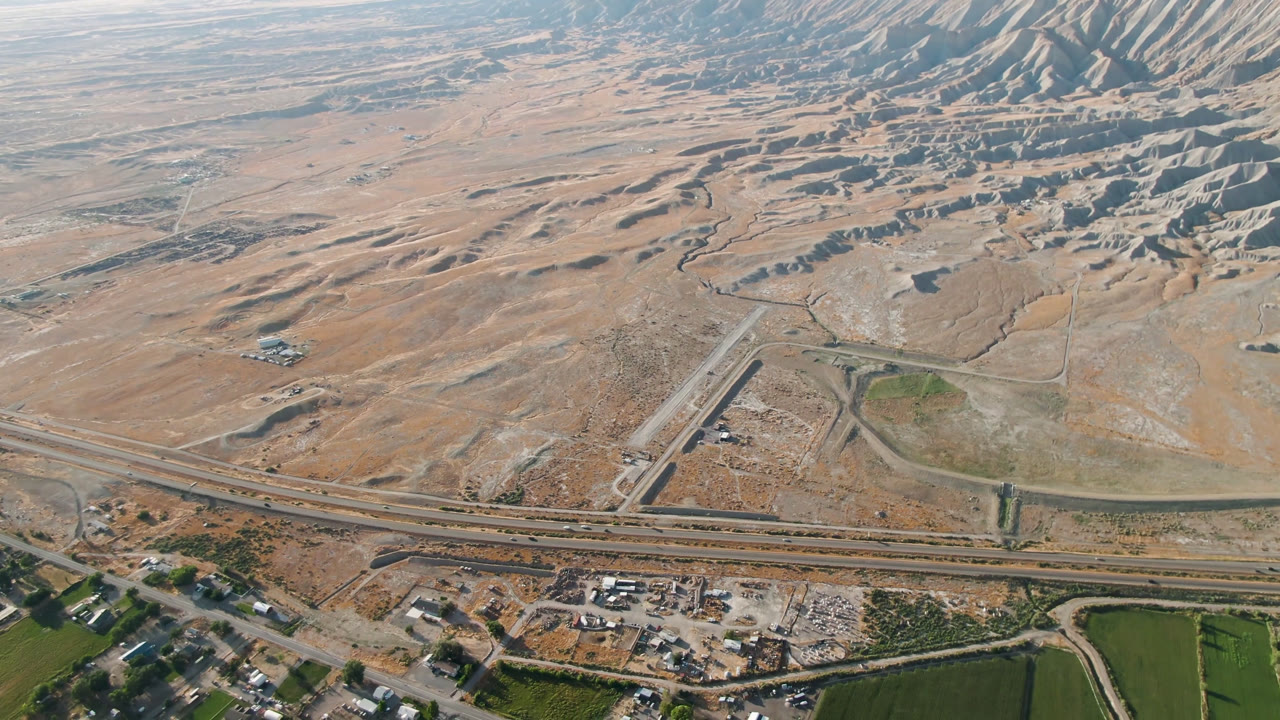 Wide aerial view in Palisades, Colorado showing highway infrastructure, small building clusters, dry washes, ridged hills, and no visible people.