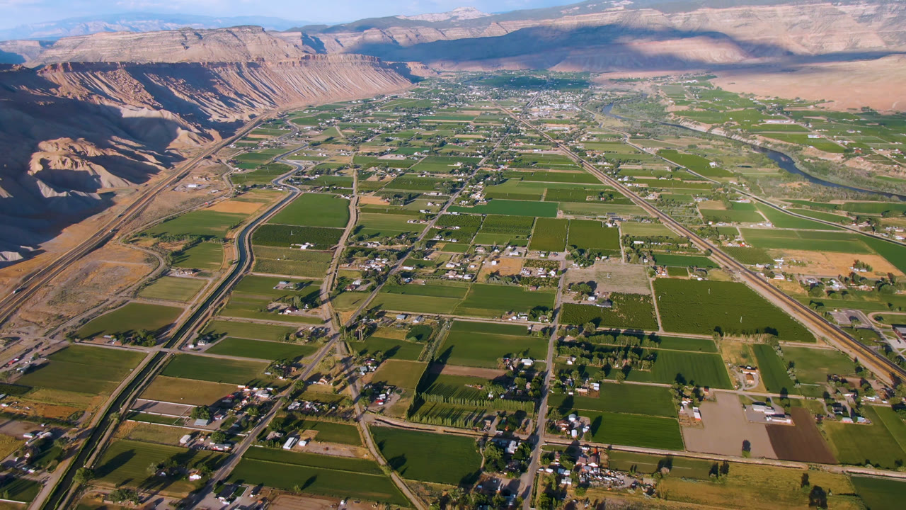 Second aerial frame over Palisades, Colorado, showing more central valley fields, clustered buildings, straight roads, a corridor along the left slope, and no visible people.