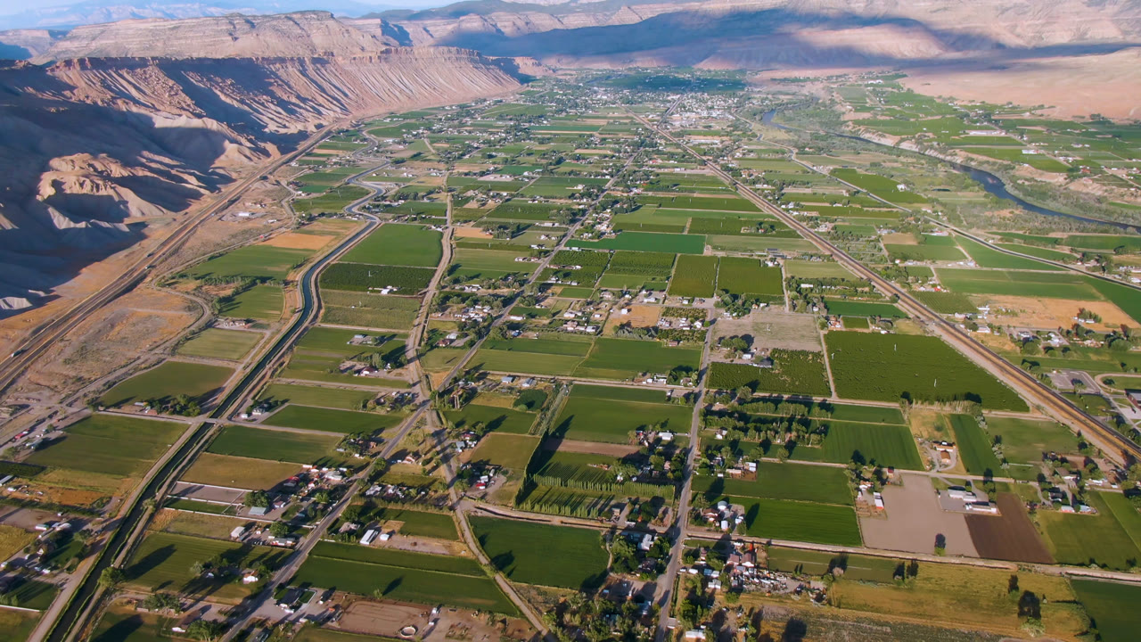 Aerial view of rectangular farmland, road network, town buildings, cliffs, and mountains.