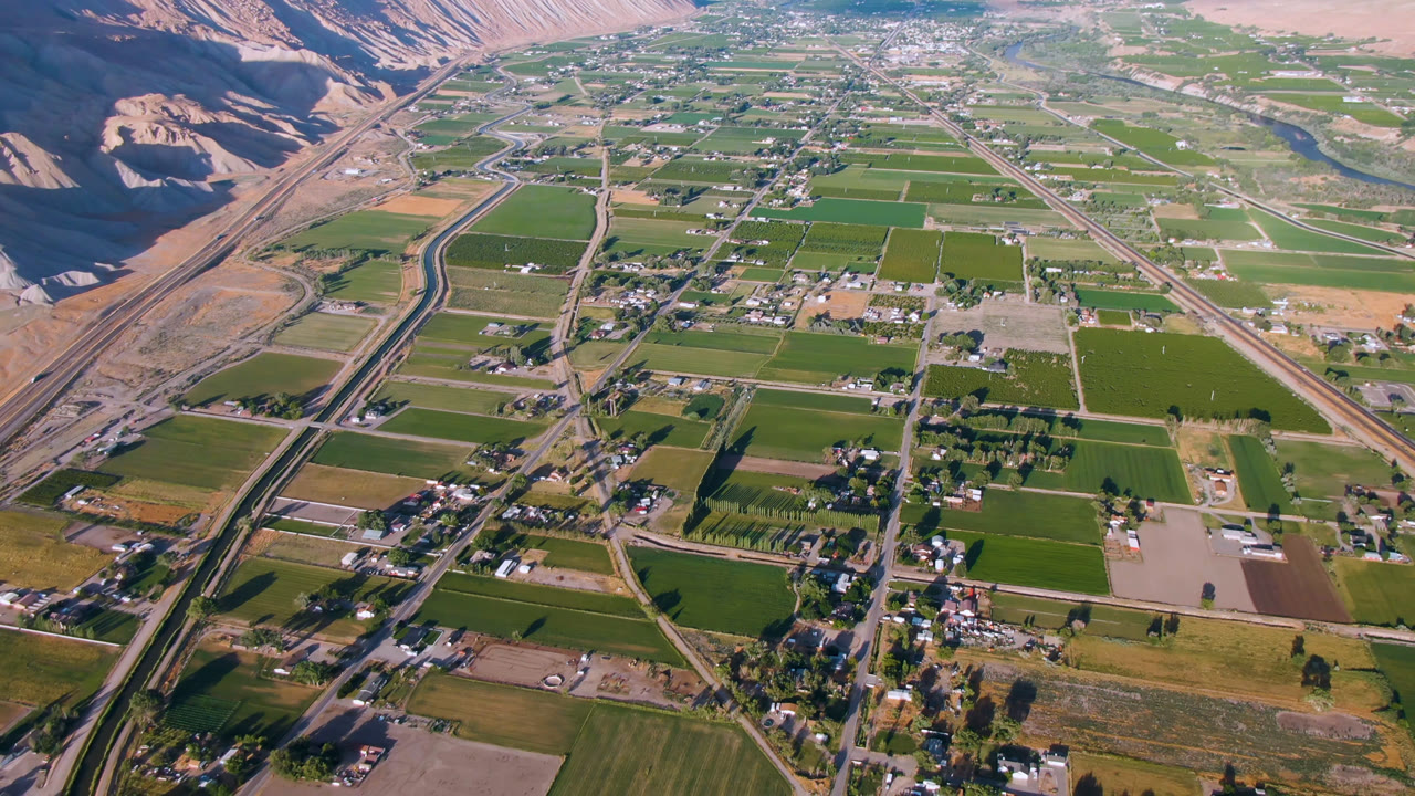 Aerial view of green fields, rural roads, houses, and dry valley hills.