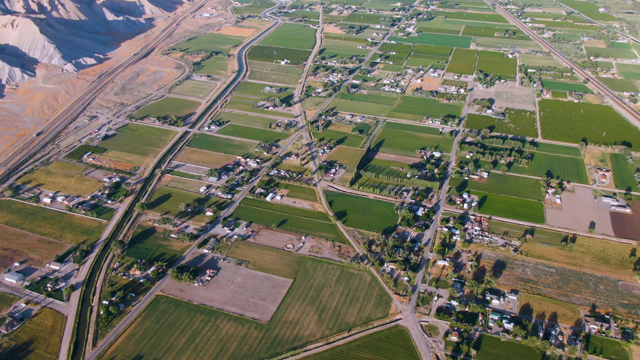 Aerial view of green fields, roads, houses, and dry hills.