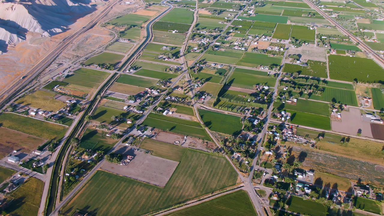 Second frame over Palisades, Colorado, showing a denser cluster of buildings near intersecting roads, broad green fields, the highway corridor, and no visible people.