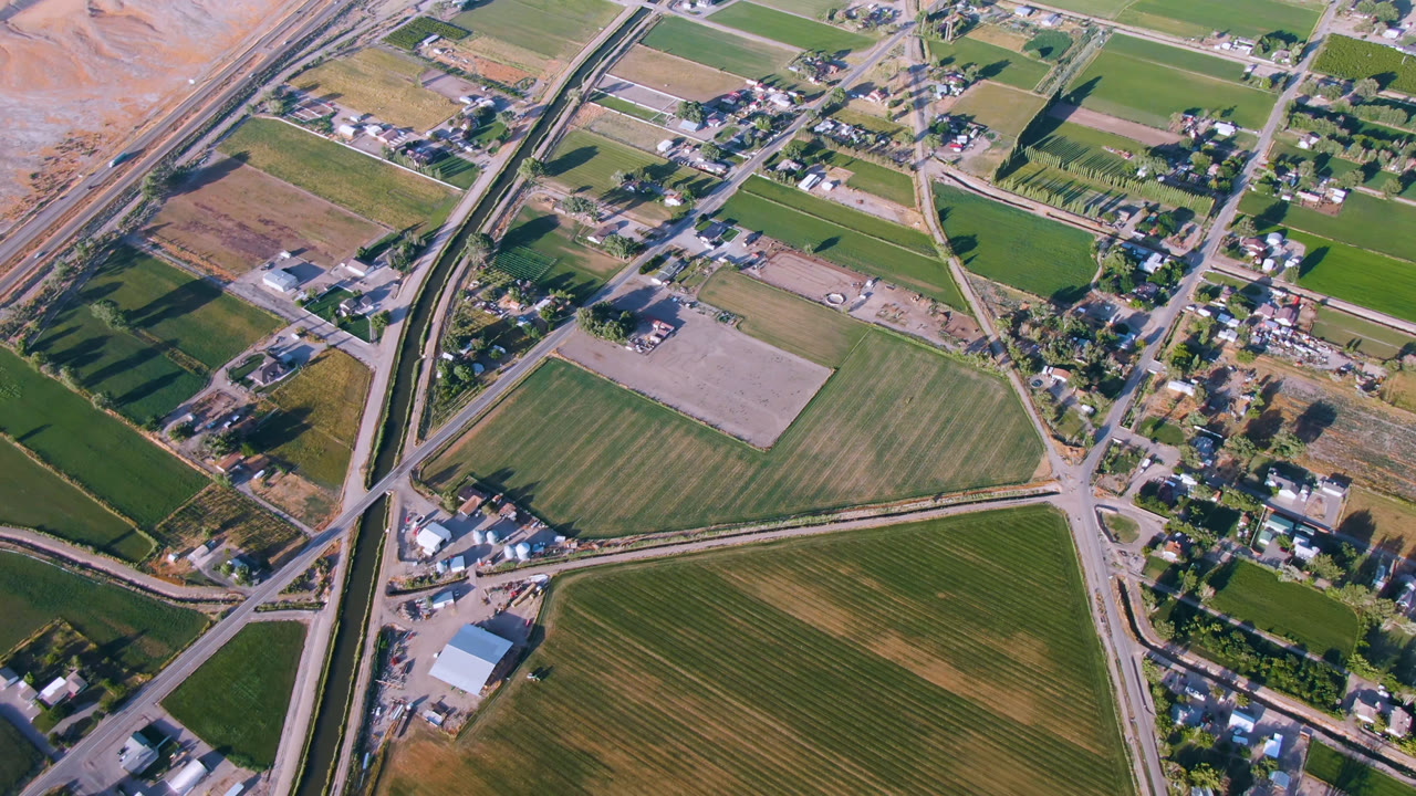 Aerial frame over Palisades, Colorado, showing rectangular green and tan fields, a curving road network, small building clusters, dry hillside, and no visible people.