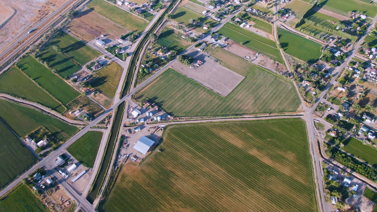 Overhead view of fields, roads, buildings, and a narrow waterway.