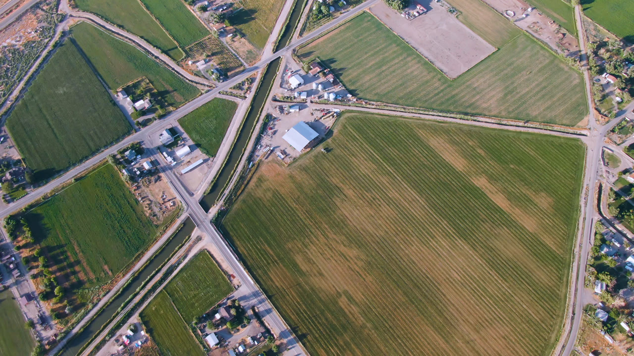 Overhead frame from Palisades, Colorado showing green and tan fields divided by rural roads, scattered buildings, trees, and no visible people.