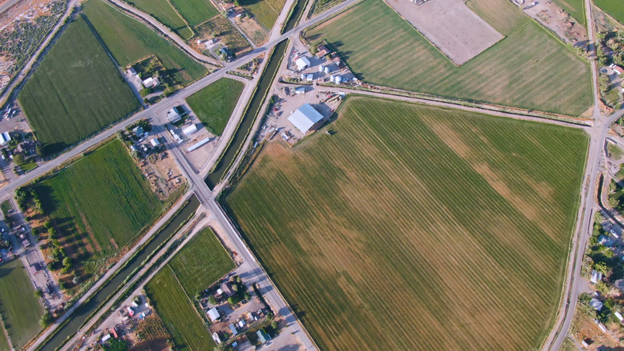 Top-down rural landscape with crop rows, roads, and buildings.