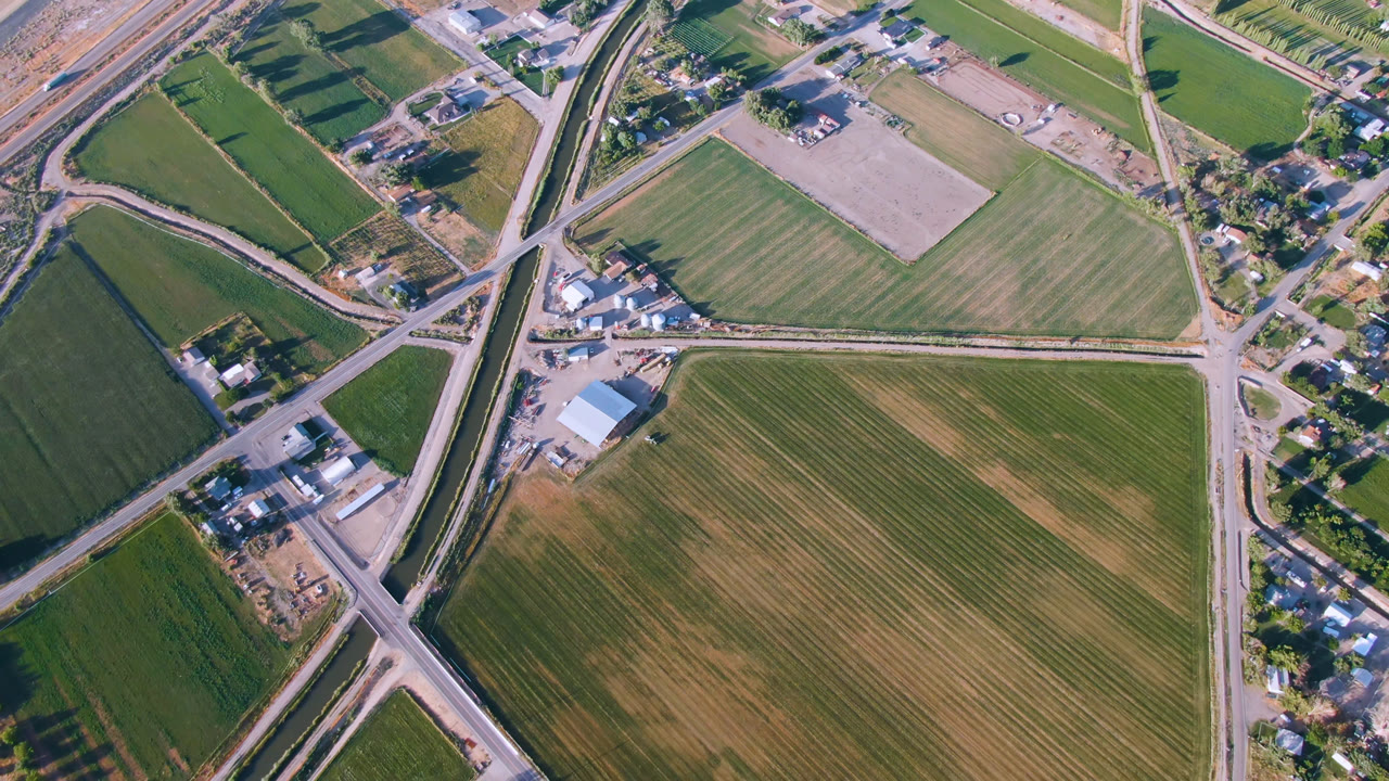 Overhead aerial view in Palisades, Colorado showing green and tan fields, crossing rural roads, scattered buildings, trees, and no visible people.