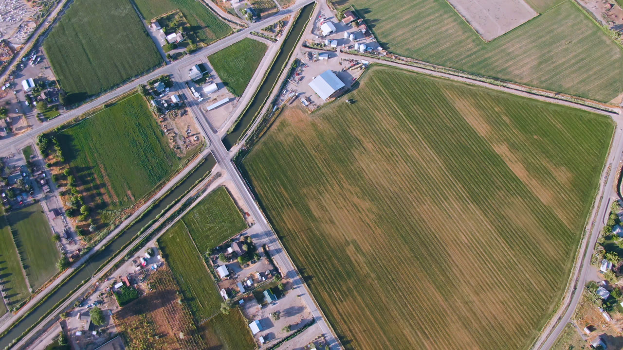 Overhead aerial frame in Palisades, Colorado, showing green and tan farm fields divided by roads, a diagonal highway, scattered buildings, trees, and no visible people.