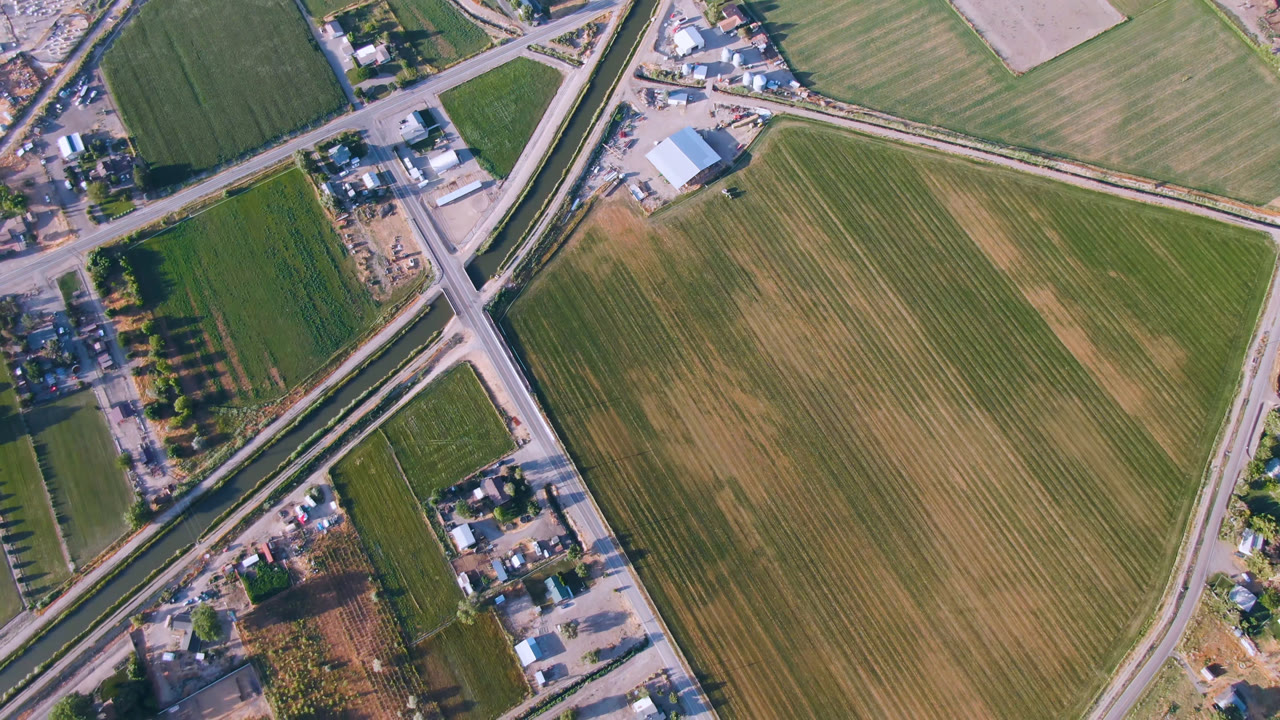 Aerial frame in Palisades, Colorado, with a road junction near the upper left, a large striped field filling the right side, small structures, trees, and no visible people.