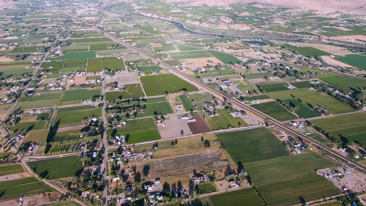 Second frame over Palisades, Colorado with green crop blocks, pale cleared parcels, a diagonal roadway, adjacent rail line, clusters of homes or farm buildings, and no visible people.