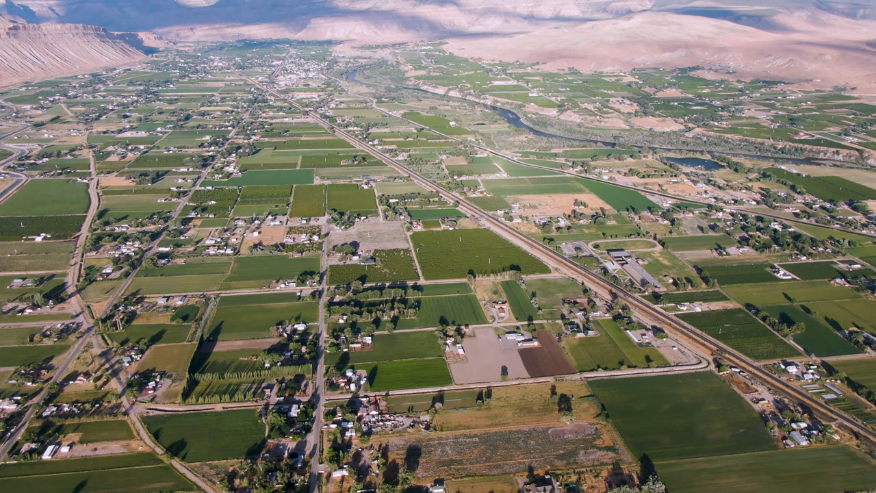 Aerial view of farm fields, roads, town buildings, river corridor, and distant mountains.