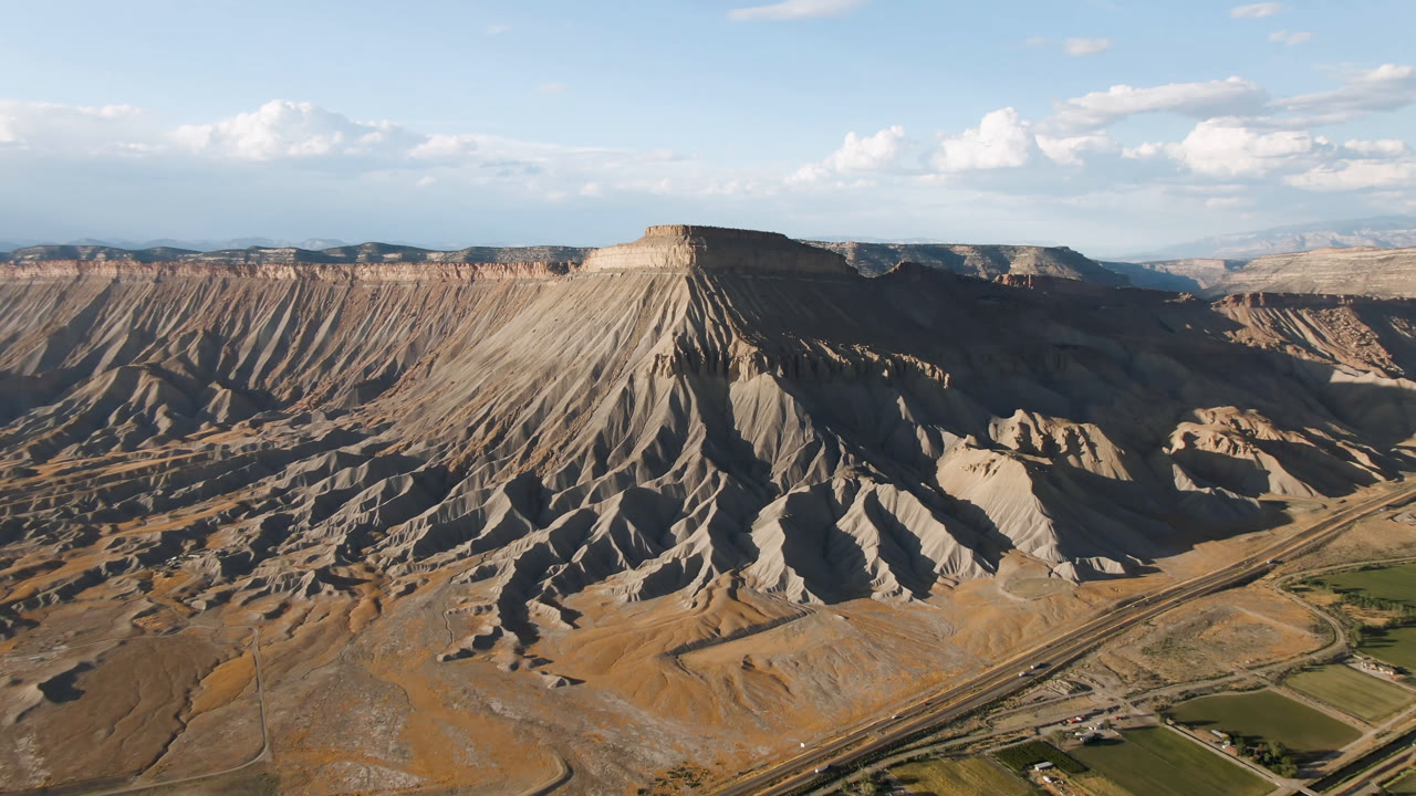 Eroded mesa slopes with roads and green fields below.
