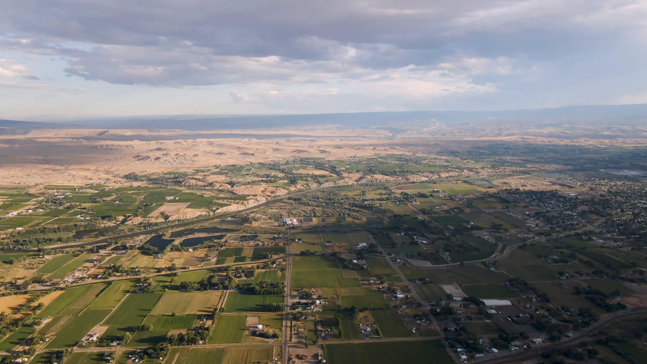 High aerial view of green fields, roads, settlement, desert flats, and cloudy sky
