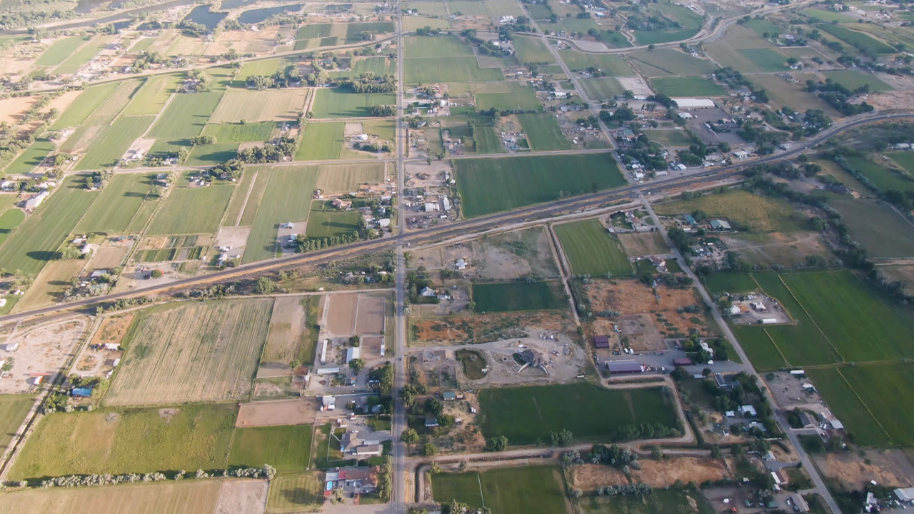 Aerial view of fields, roads, buildings, rail line, and water edge.