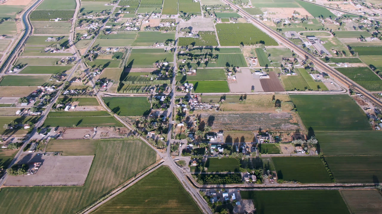 High aerial frame over Palisades, Colorado showing green and tan farm fields, a diagonal highway, smaller roads, tree rows, scattered buildings, and no visible people.