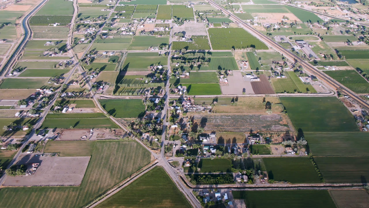 Second aerial frame over Palisades, Colorado with rectangular fields, a diagonal highway corridor, clustered rural buildings, trees, and no visible people.