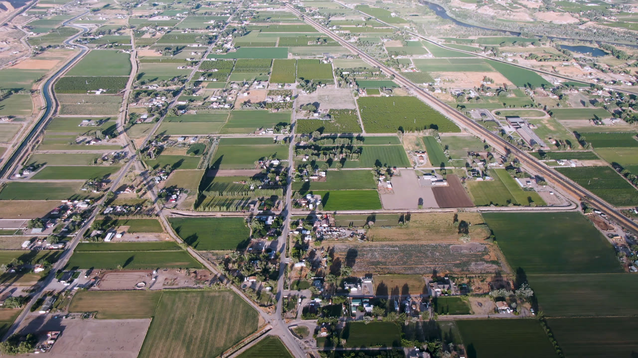 Aerial view over farm fields, roads, scattered homes, and distant river valley.