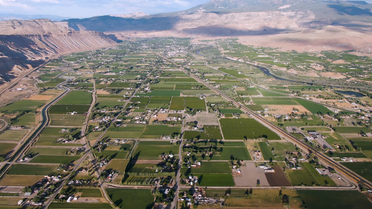 Aerial view over a green valley with roads, farms, buildings, and mountains.