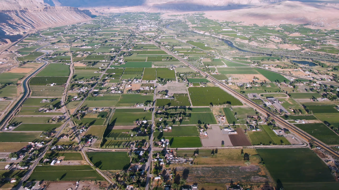 Aerial view of farm fields, roads, buildings, and mountains beyond a valley town.