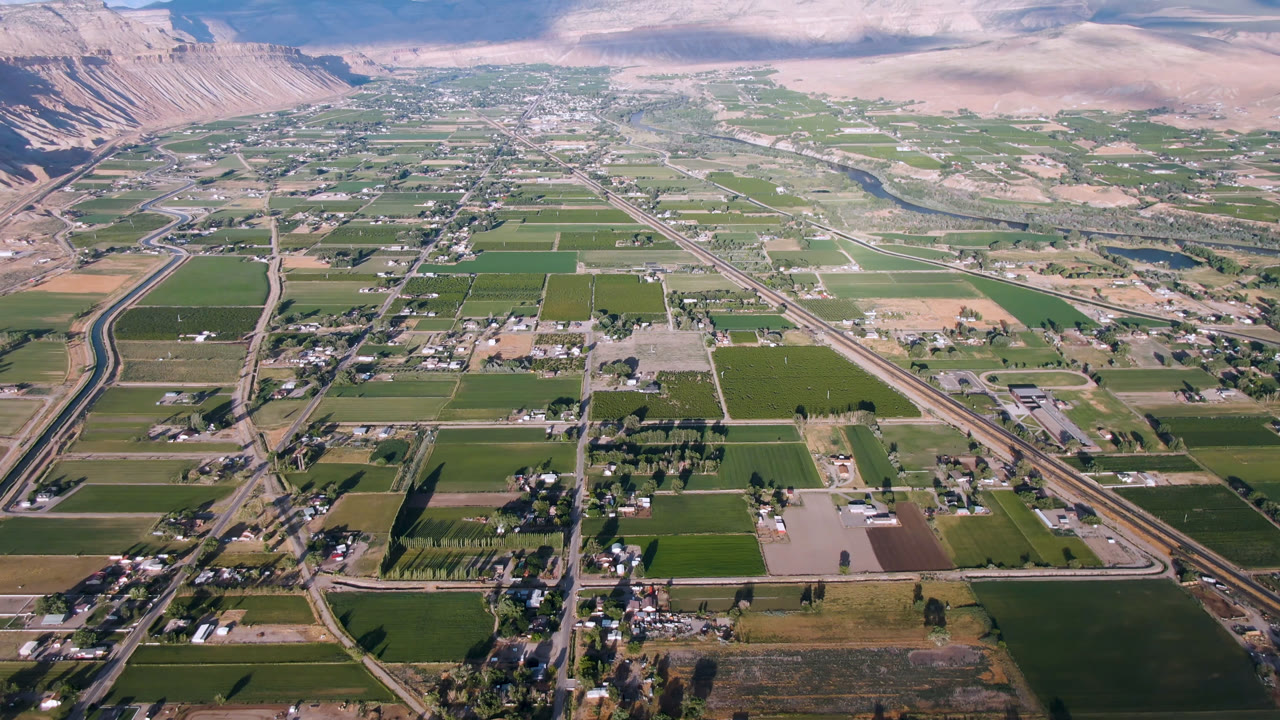 Second aerial frame of Palisades, Colorado, showing a broader stretch of rectangular fields, rural roads, scattered homes, distant mountains, and no visible people.