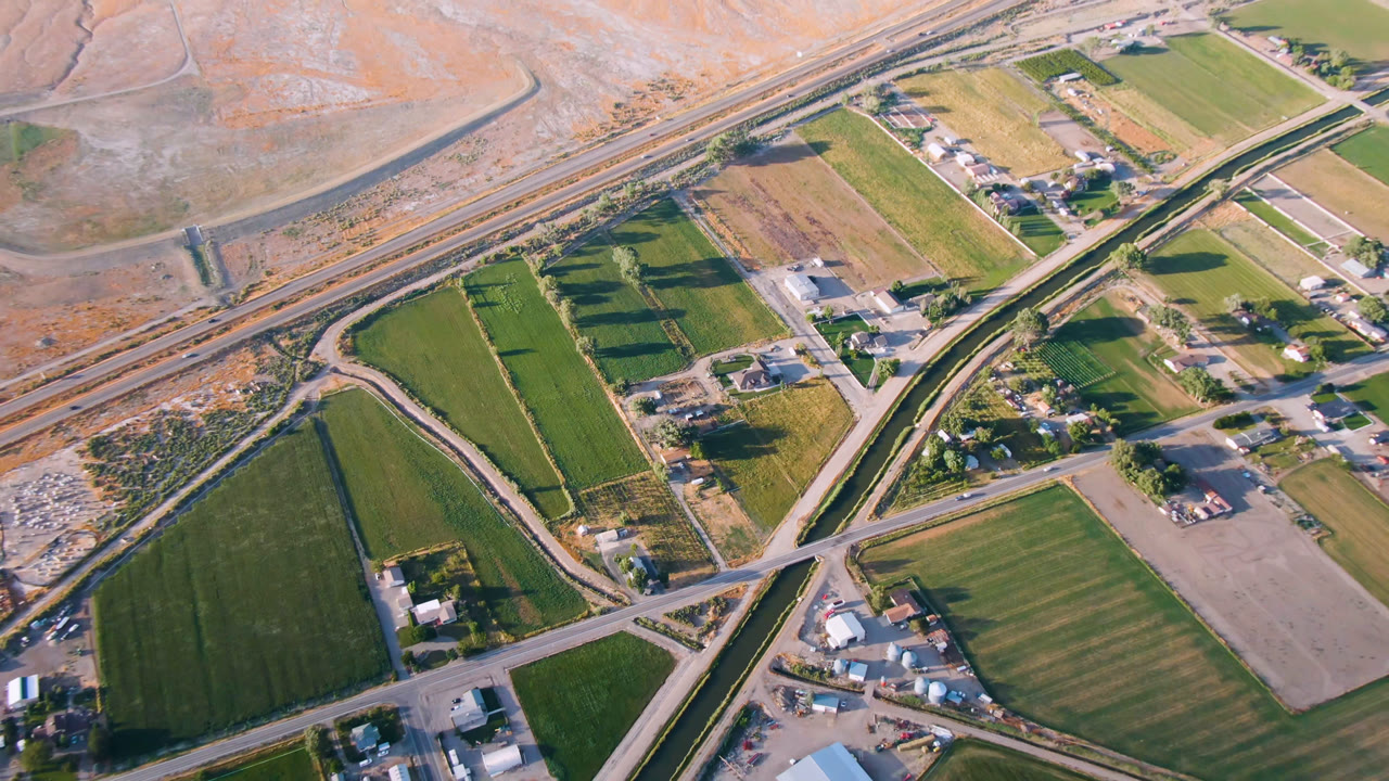 Aerial view of rural fields, roads, buildings, highway, and a winding water channel.