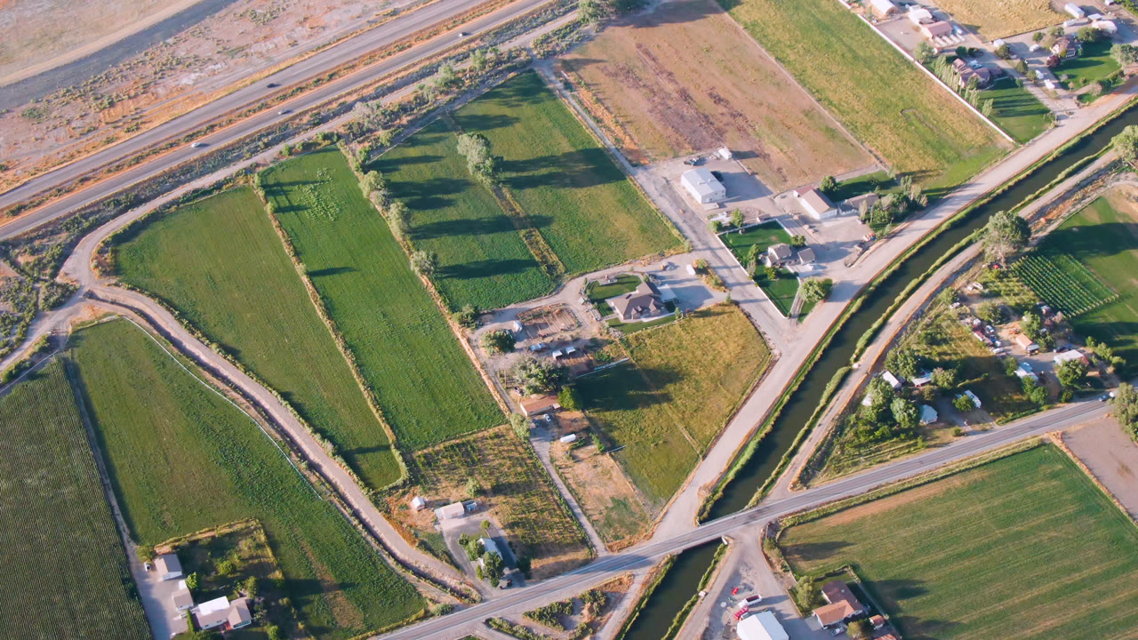 Aerial view over rural Palisades, Colorado showing rectangular green fields, diagonal paved roads, a narrow water channel, scattered buildings, a highway at the top edge, and no visible people.