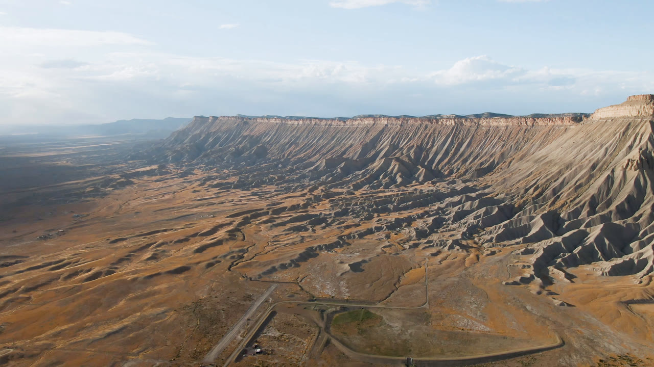Aerial view in Palisades, Colorado, with pale ridged slopes on the right, orange-brown terrain below, a small road junction near the bottom, and no visible people.