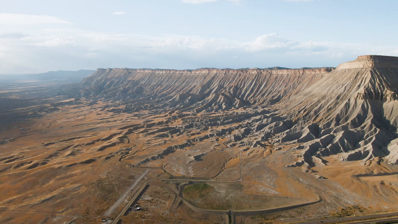 Second frame of Palisades, Colorado with the mesa wall stretching across the background, branching road lines below, dry ground, and no visible people.