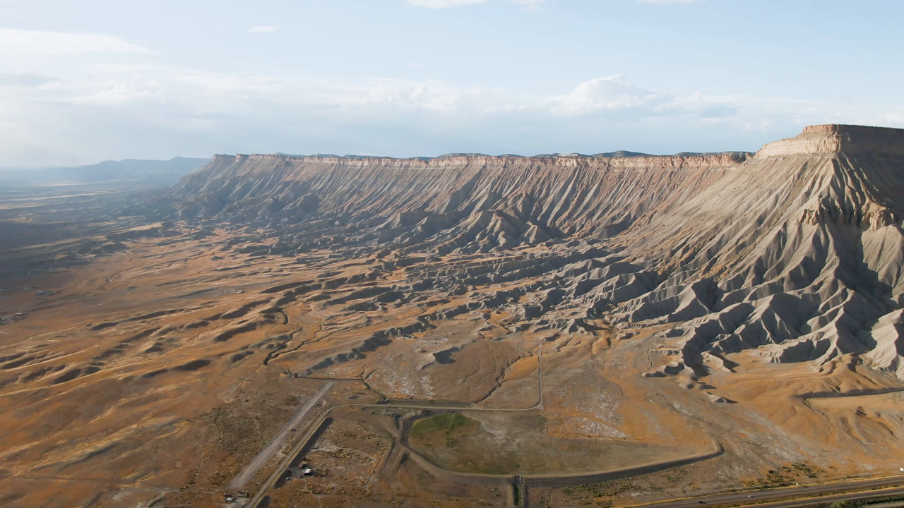 Large mesa formation with shadowed gullies and road at the base
