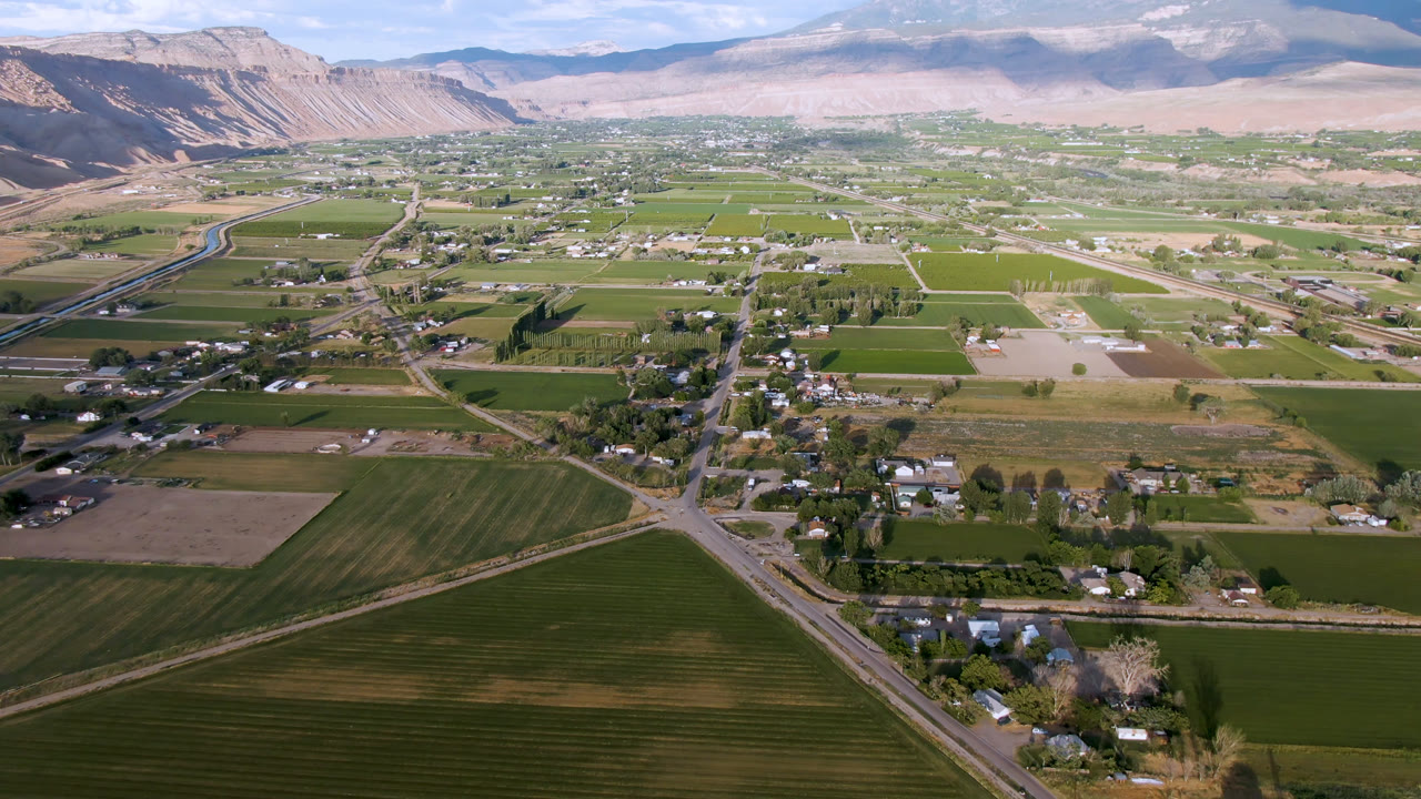 Wide drone view of agricultural blocks, a small town, and mountains under daylight.