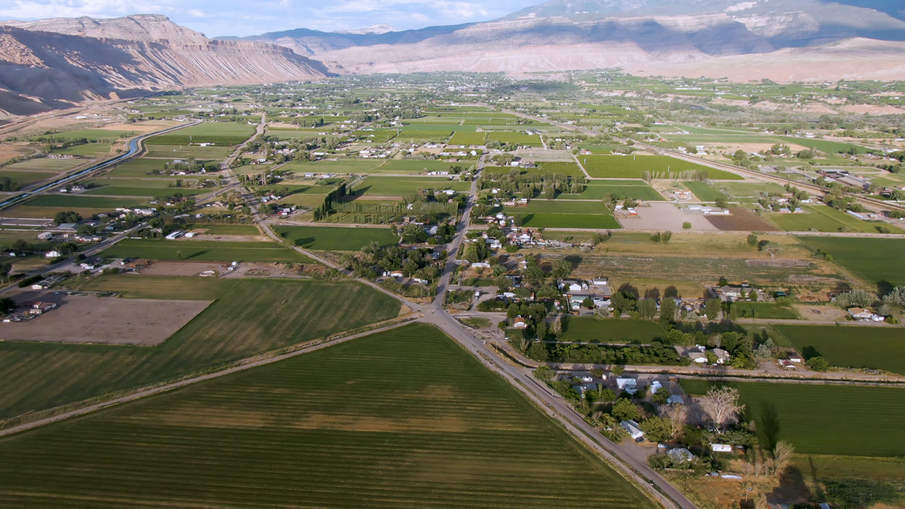 Aerial view over fields, roads, buildings, and distant mountains.