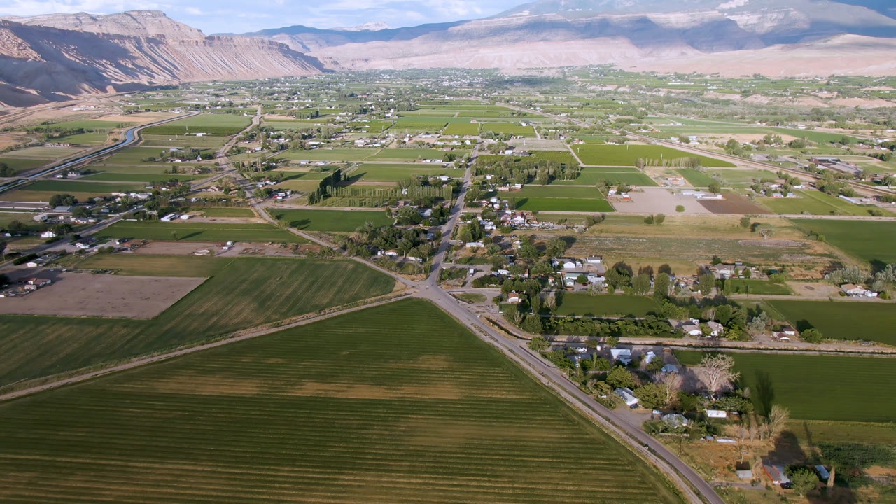 Aerial view of green fields, rural roads, scattered buildings, and mountains.