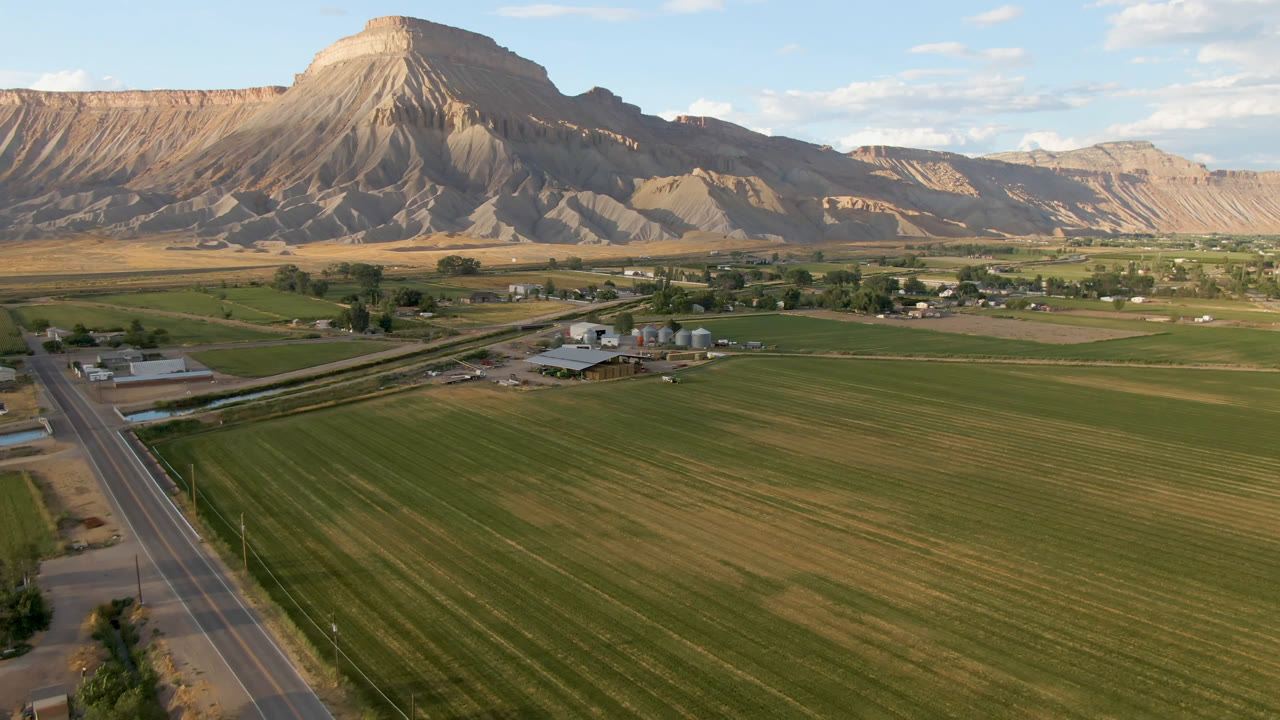 Second frame of the Palisades, Colorado aerial view, with the road running up the left side, striped farm fields below, low buildings near center, and no visible people.