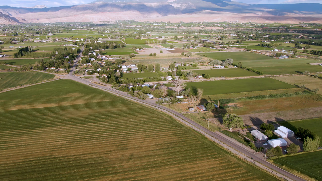 Aerial view of farm fields, road, rural buildings, and distant mountains.