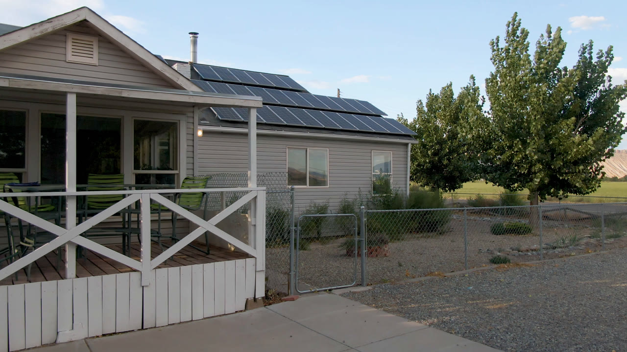 Small house with rooftop solar panels beside a porch and trees