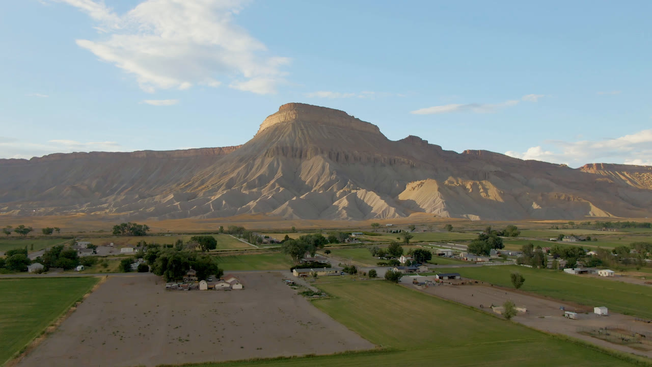 Wide opening frame over Palisades, Colorado fields and scattered buildings, with a flat-topped mesa ridge across the horizon and no visible people.