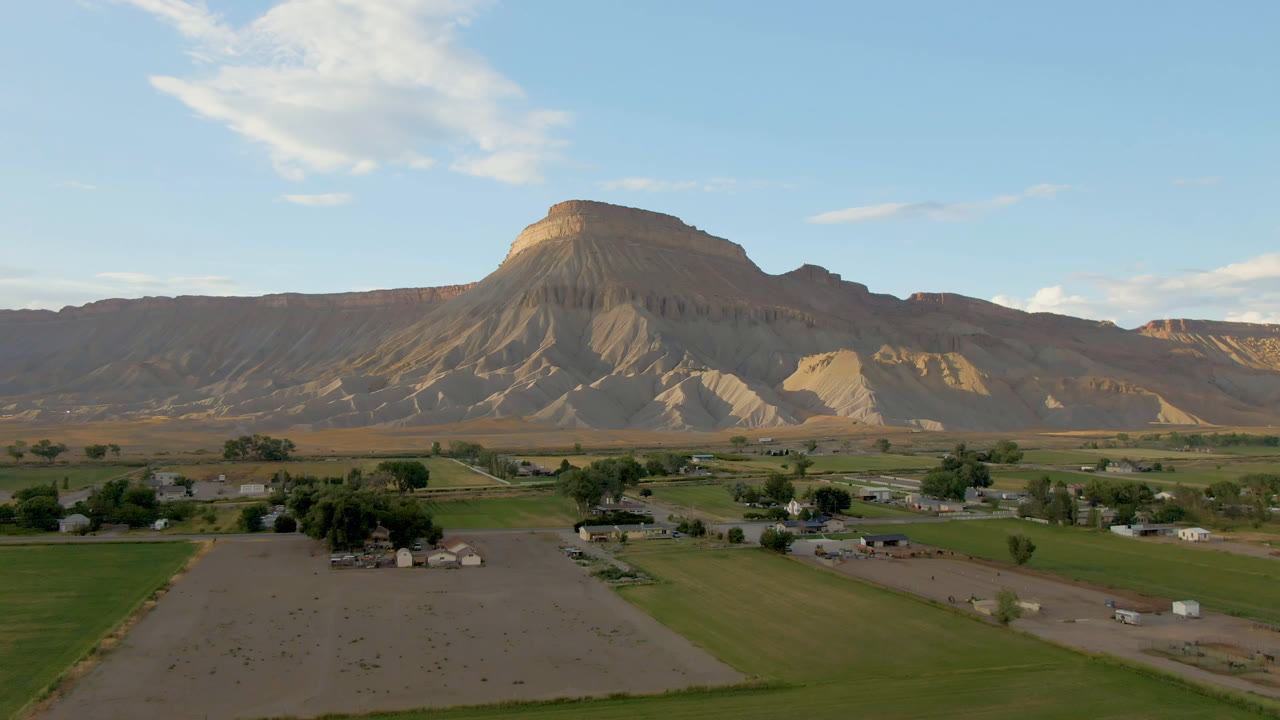 Second frame holds the Palisades, Colorado valley view with green parcels, a pale dirt field, low buildings, and sunlit mesa walls in the background, with no visible people.